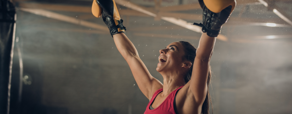 Female athlete wearing boxing gloves holds her hands up in victory 