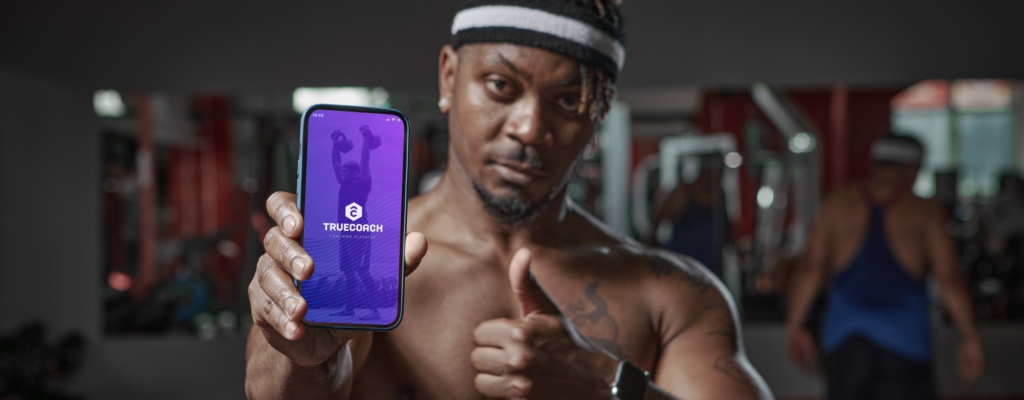 Male fitness coach holds up a phone with the trueCoach logo and a thumbs up