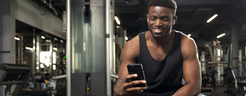 A man in the gym is sitting down and smiling at his phone 