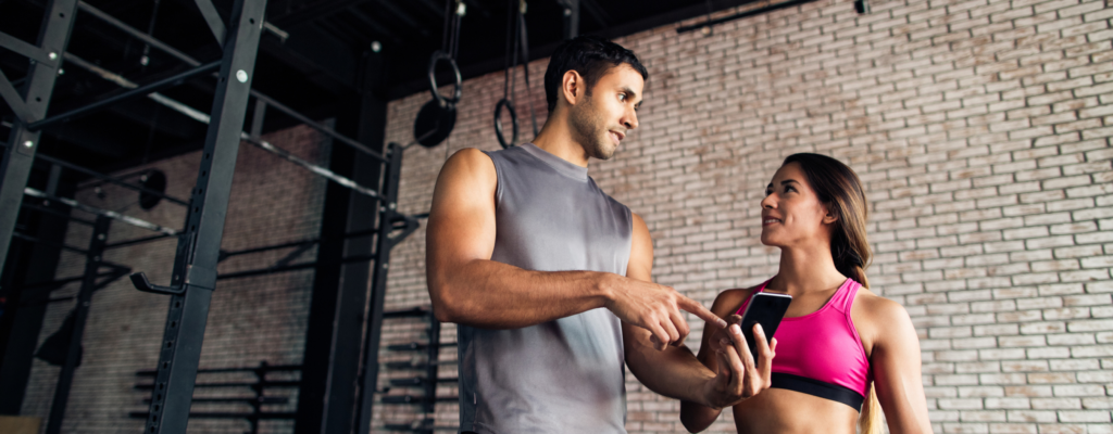 A man and a women are having a conversation in a gym while looking at a phone screen