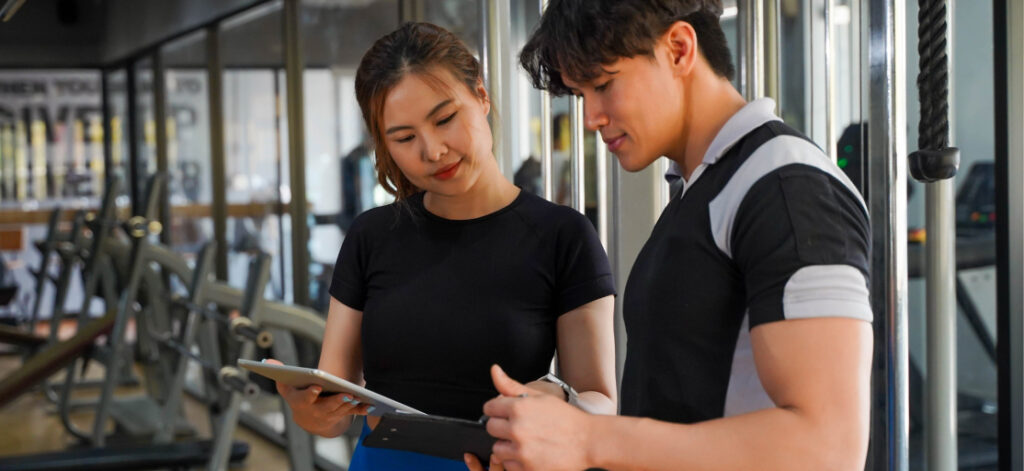 Image of personal trainer showing a colleague a guide to selling high-ticket programs